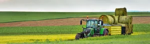 En traktor med ett släp med ensilagebalar. Öppna fält runtomkring